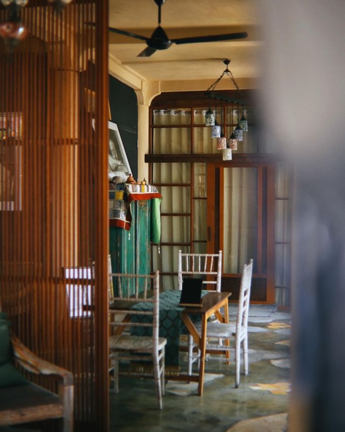 Dining room seen through wooden slats, with white chairs under a ceiling fan