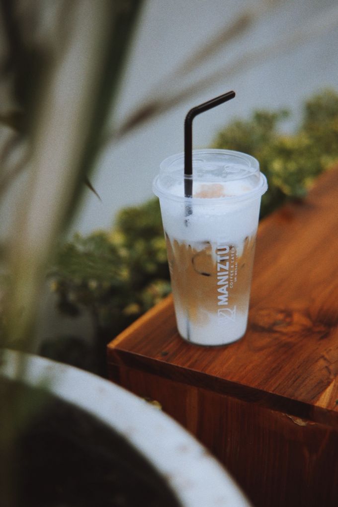 Iced latte in a Maniztutu takeaway cup on a wooden ledge